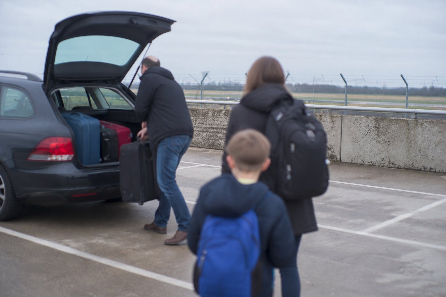 Gezin laadt koffers uit de auto op een parkeerdek bij een regionale luchthaven